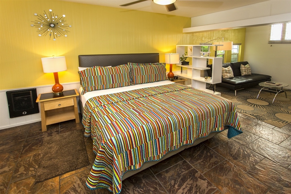 A wide view of a hotel room with a bed, nightstand, lamp, and couch.