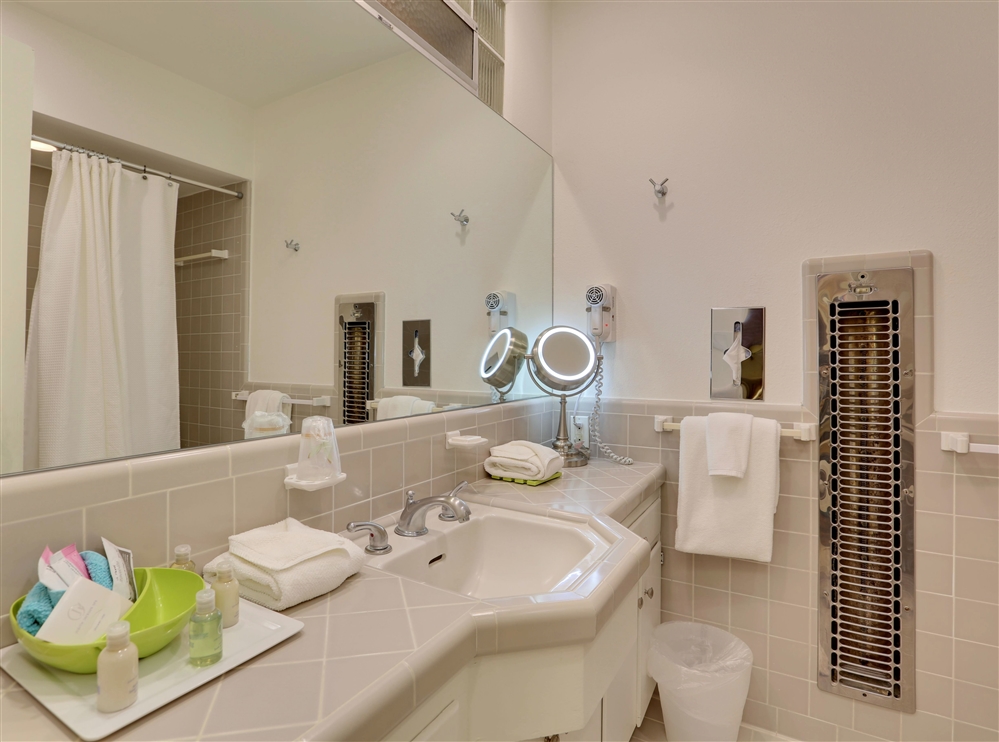 A clean bathroom with a sink, mirror, towels, and toiletries.