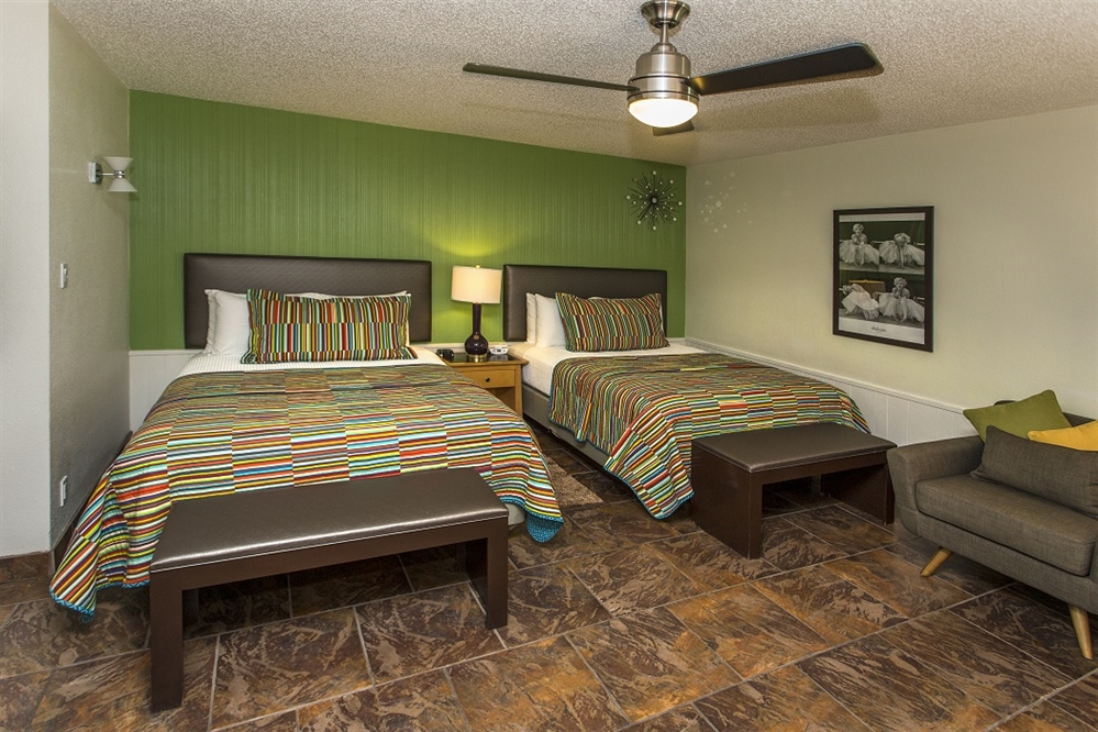 A hotel room with two beds, a chair, and a nightstand.