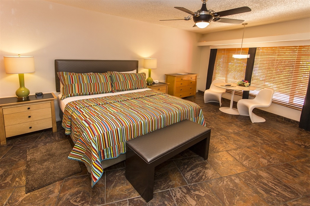 A wide view of a hotel room with a bed, nightstands, a dresser, a desk with chairs, and a ceiling fan.