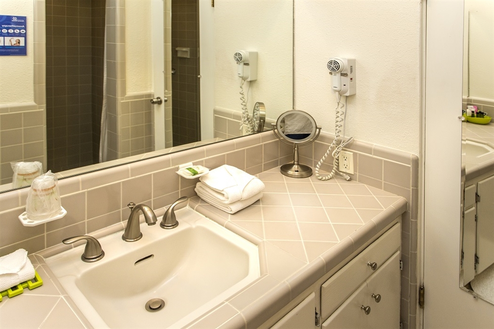 A hotel bathroom sink area with a large mirror, tiled backsplash, and amenities.