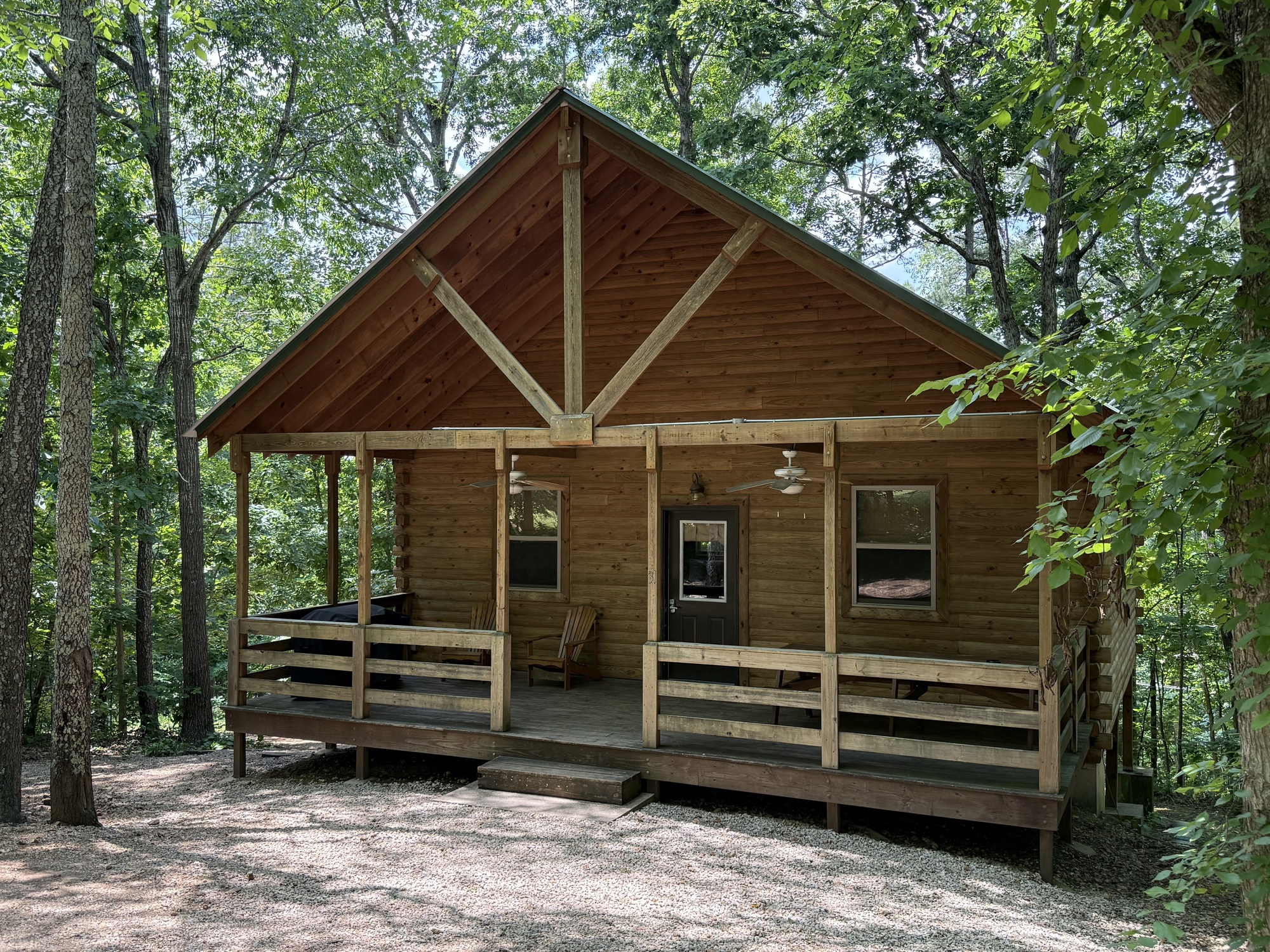 A wooden cabin with a green roof and porch, surrounded by trees.